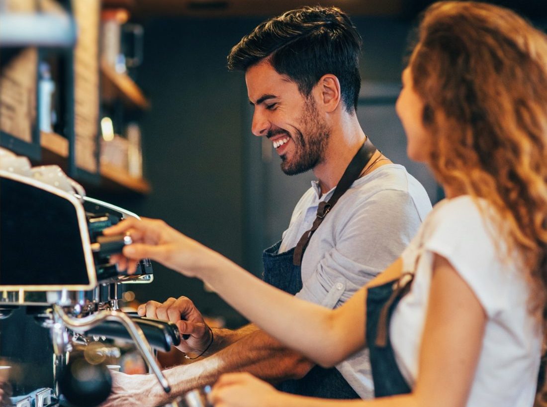Zwei Baristas lachen gemeinsam an der Espressomaschine im Groove Coffee Club München — das Geschenk-Erlebnis